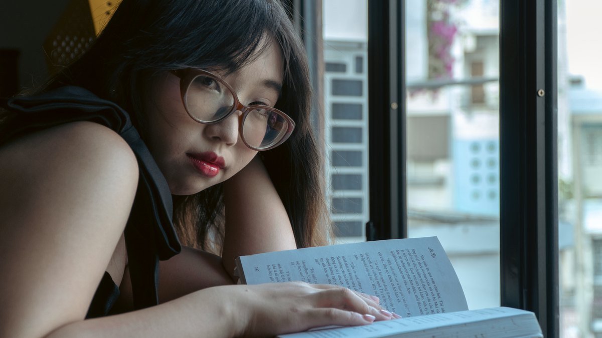 A woman reading a book beside a softly lit window